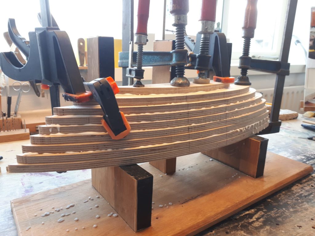 A model ship under construction on a wooden bench, wood structure visible